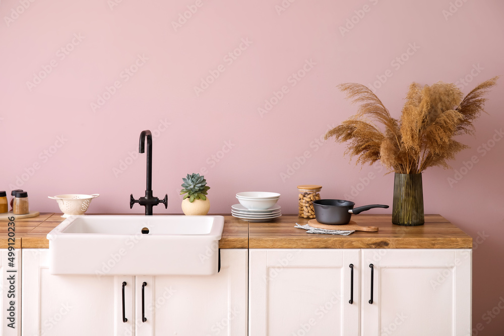 Counters with sink, kitchen utensils and pampas grass in vase near pink wall