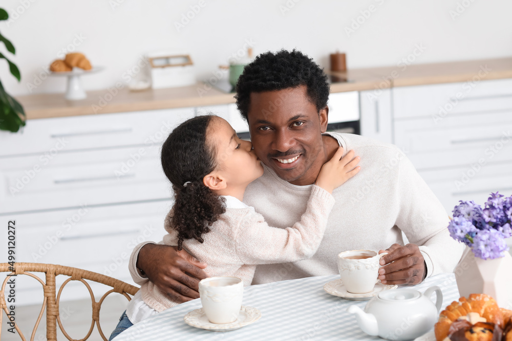 Happy little African-American girl kissing her  father in kitchen