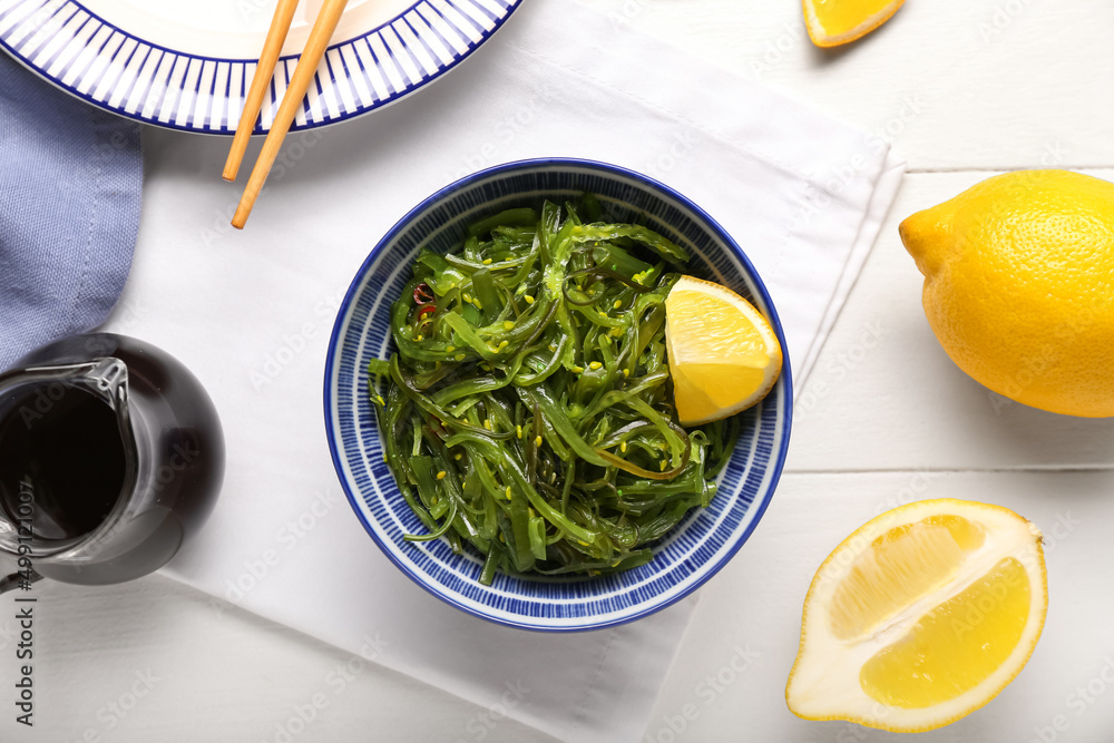 Bowl with healthy seaweed salad, sauce and lemon on light wooden background