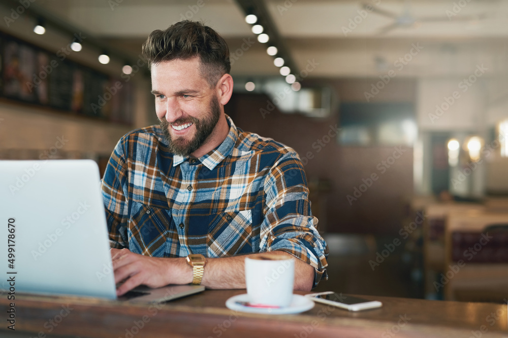 Coffee and cat videos - a classic combination. Shot of a young man using his laptop while sitting by