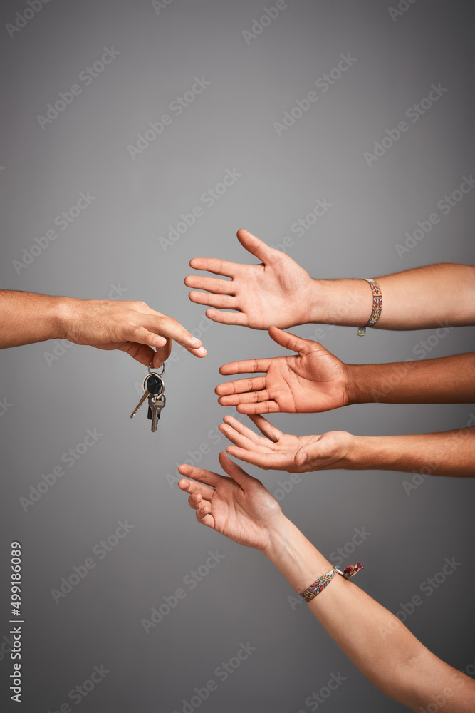 Who wants to drive. Studio shot of unidentifiable hands reaching for a set of keys against a gray ba