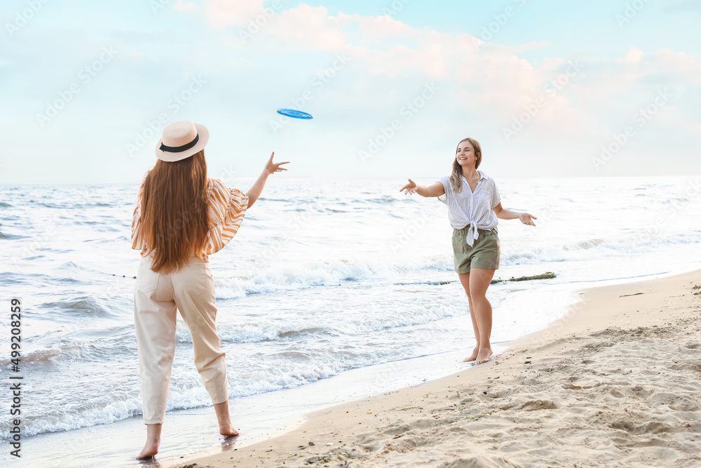 Happy young women playing frisbee on sea beach