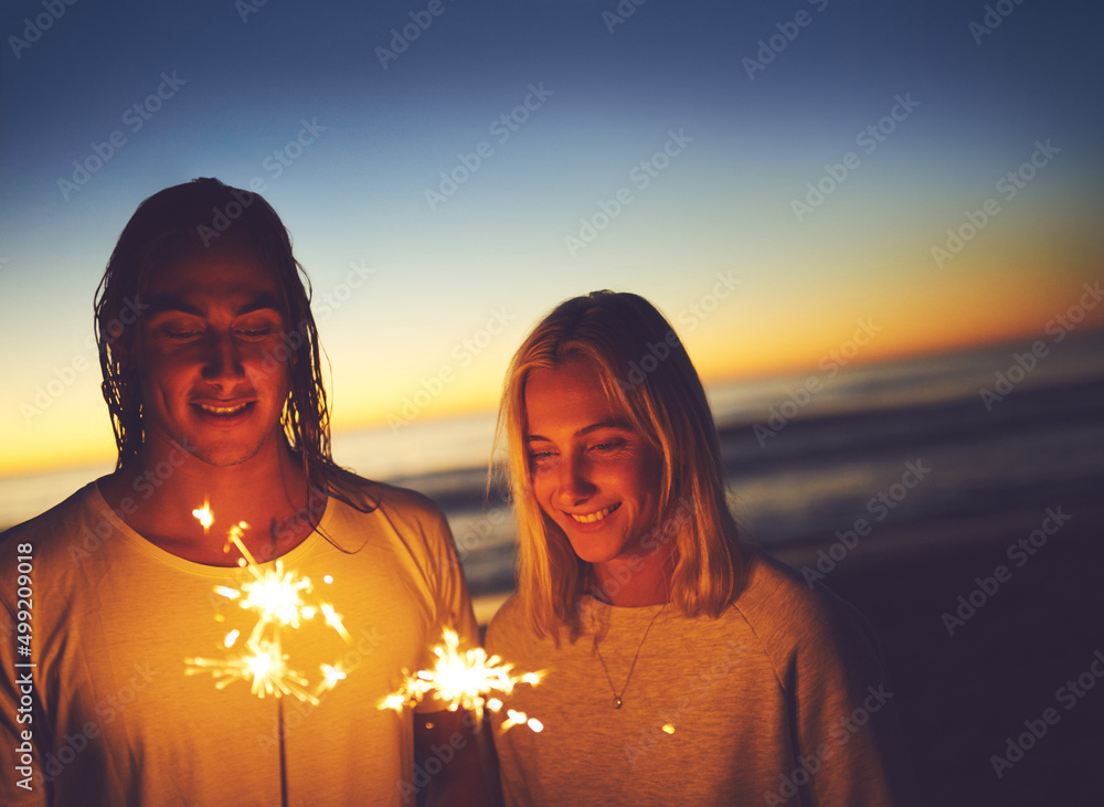 庆祝夜晚。一对年轻夫妇晚上在海滩上玩焰火的镜头。