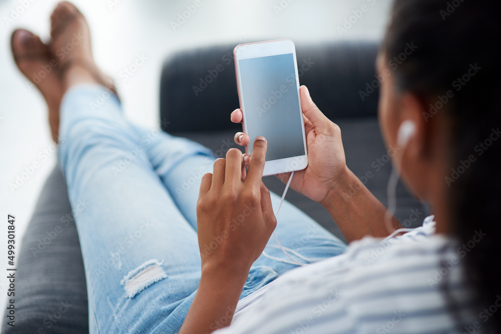 All her free time is spent online. Shot of a young woman wearing earphones while using a cellphone a