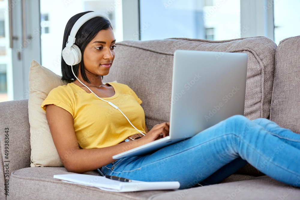 Downloading all my favourite tracks. Shot of a teenage girl listening to music and using a laptop at