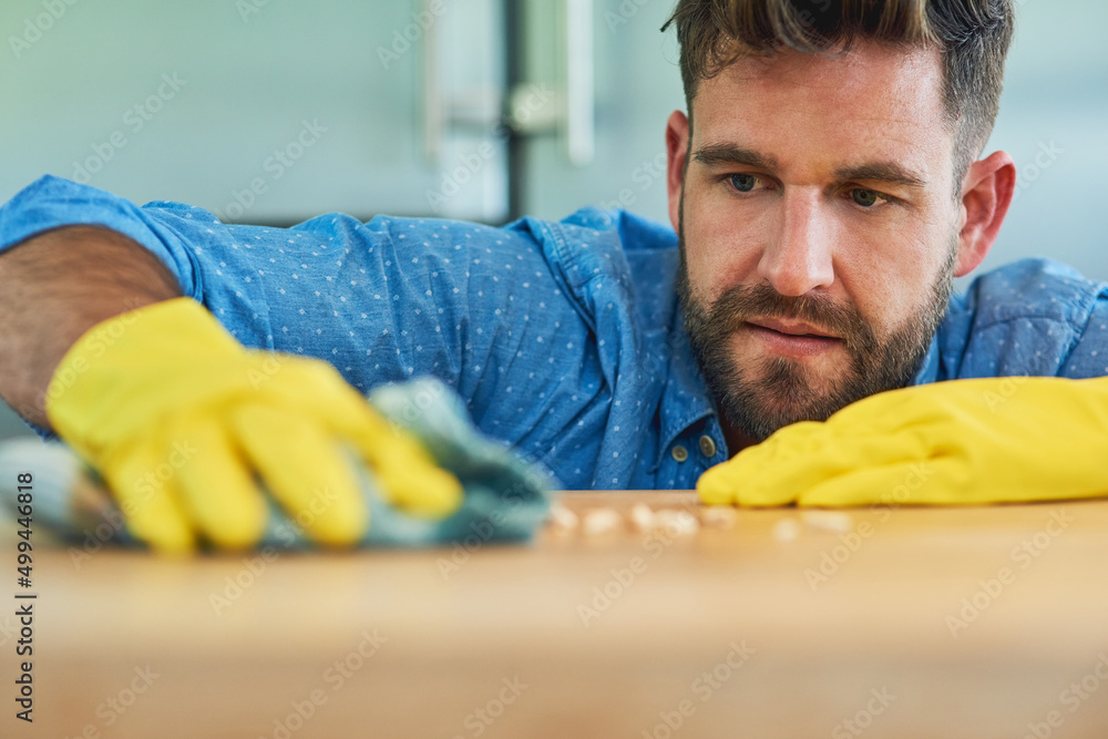 Powering through household chores like a champ. Shot of a man wearing rubber gloves while wiping a t