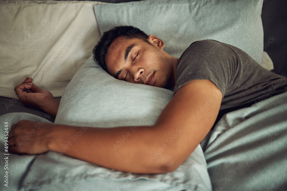 Nothing soothes the soul like a deep sleep. Shot of a young man sleeping peacefully in bed at home.