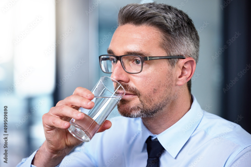 全天保持水分充足。一位成熟的商人在工作时喝一杯水的照片。