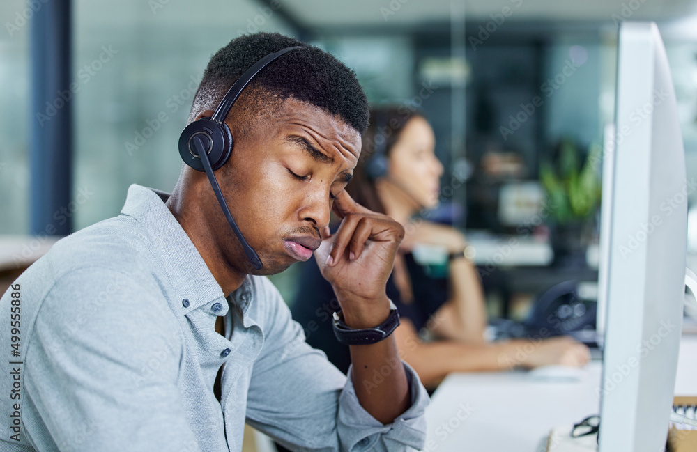 So much to get done today. Shot of a young call centre agent looking tired in an office.