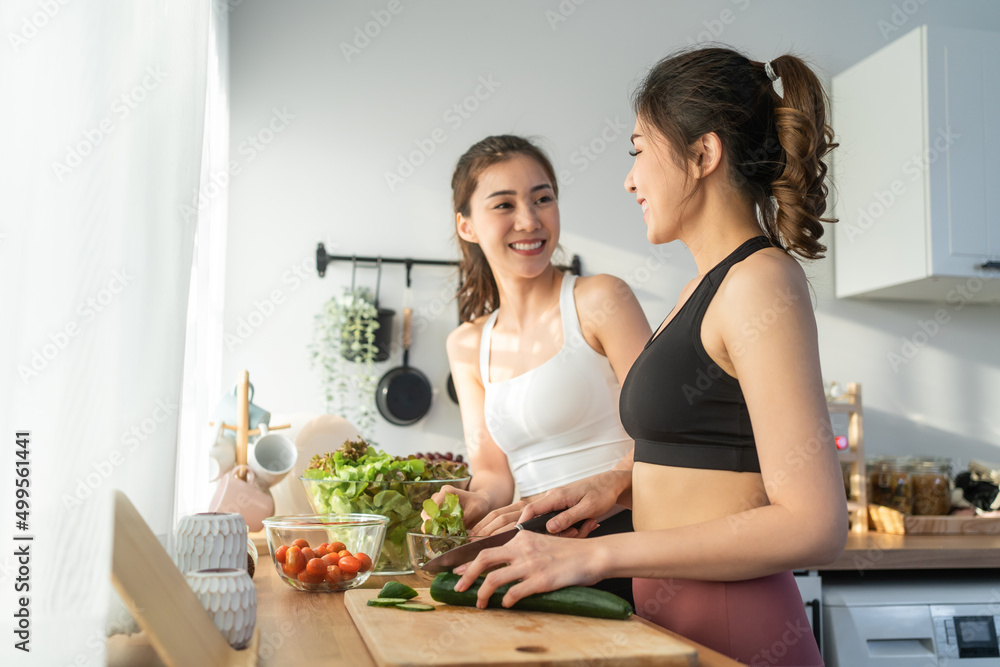 亚洲年轻的两个女人穿着运动服在厨房里做沙拉。