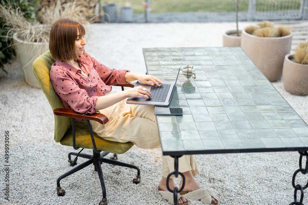 Young woman works on laptop at outdoor workspace in the garden. Concept of remote work from comforta