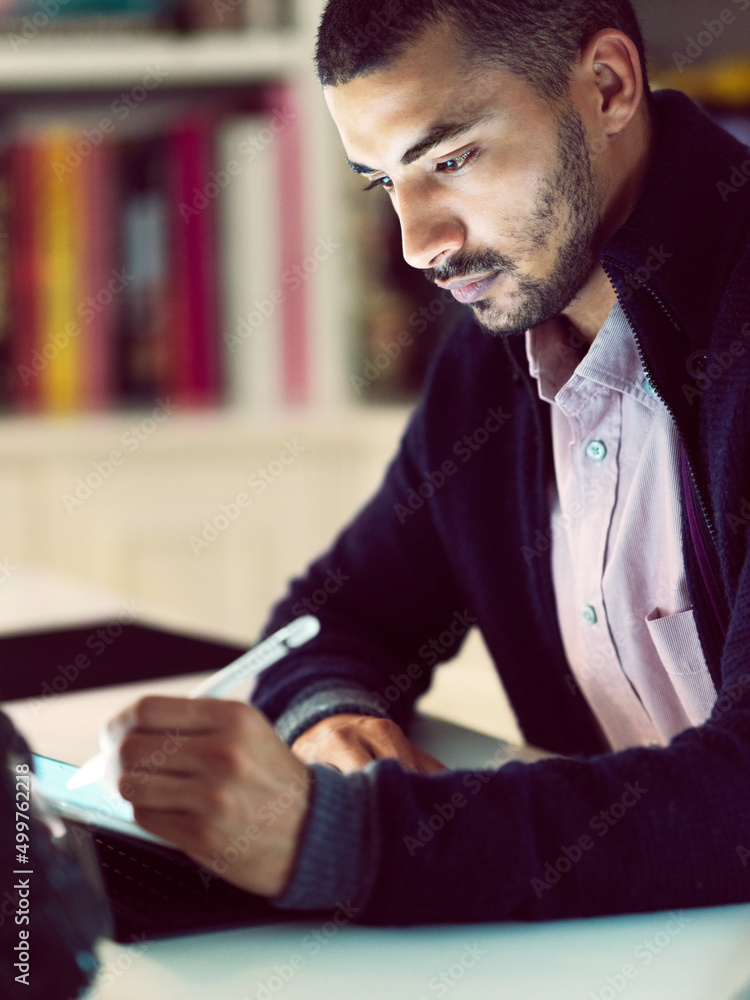 Getting down to the task at hand. Shot of a focused young man working on a digital tablet in his hom