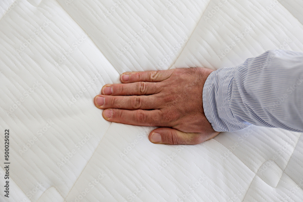 Cropped shot of man testing white orthopedic matress on firmness. Male pressing hypoallergenic foam 