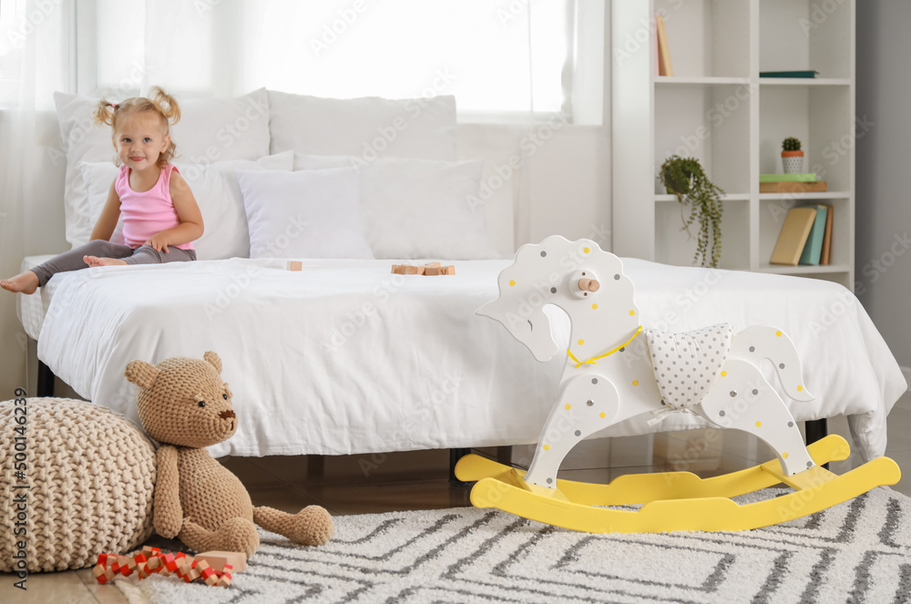 Rocking horse and toys near bed with sitting baby girl at home