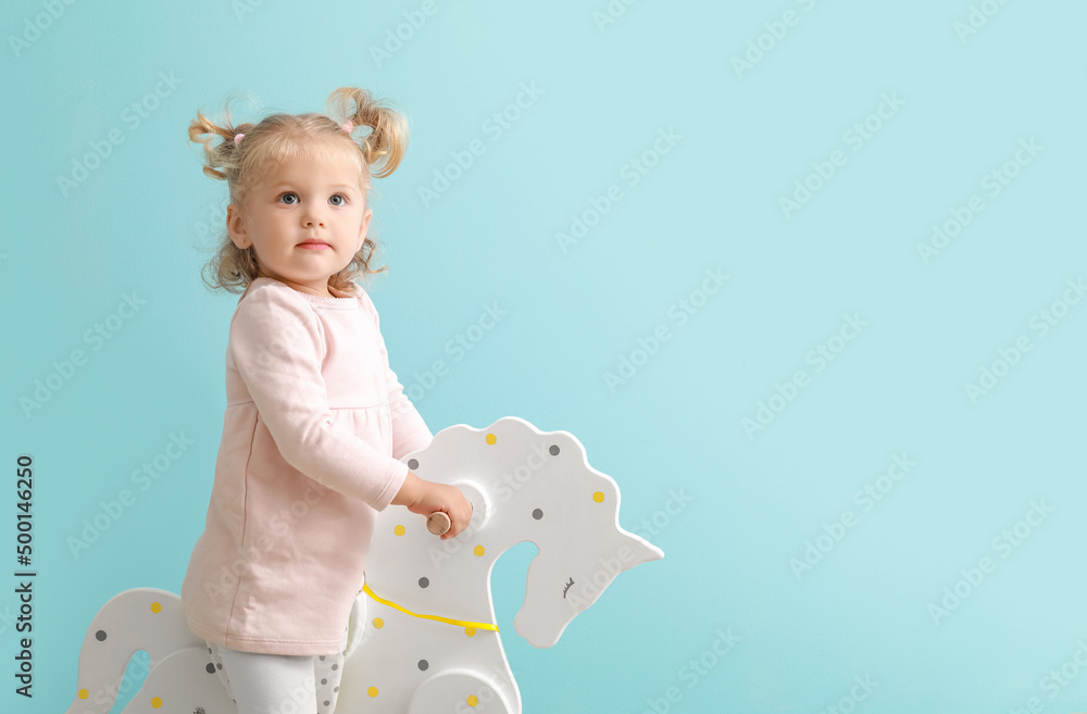 Adorable baby girl with rocking horse on blue background