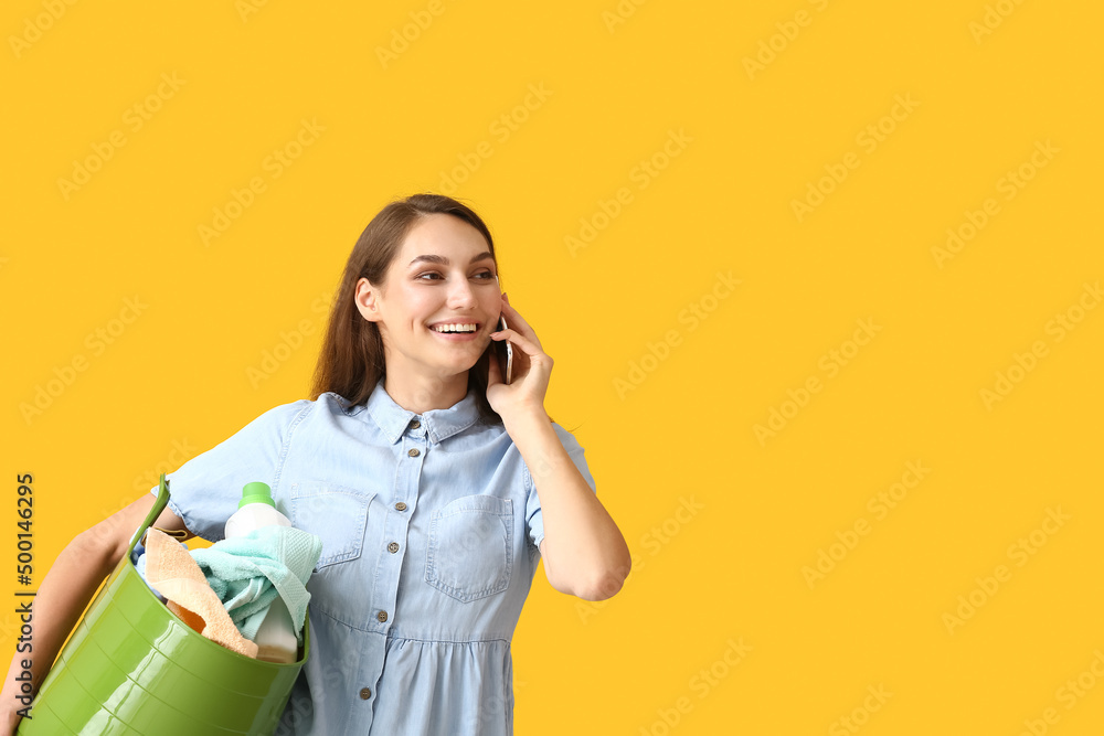 绿色篮子里装着洗好的衣服的美女在黄色背景下用手机聊天