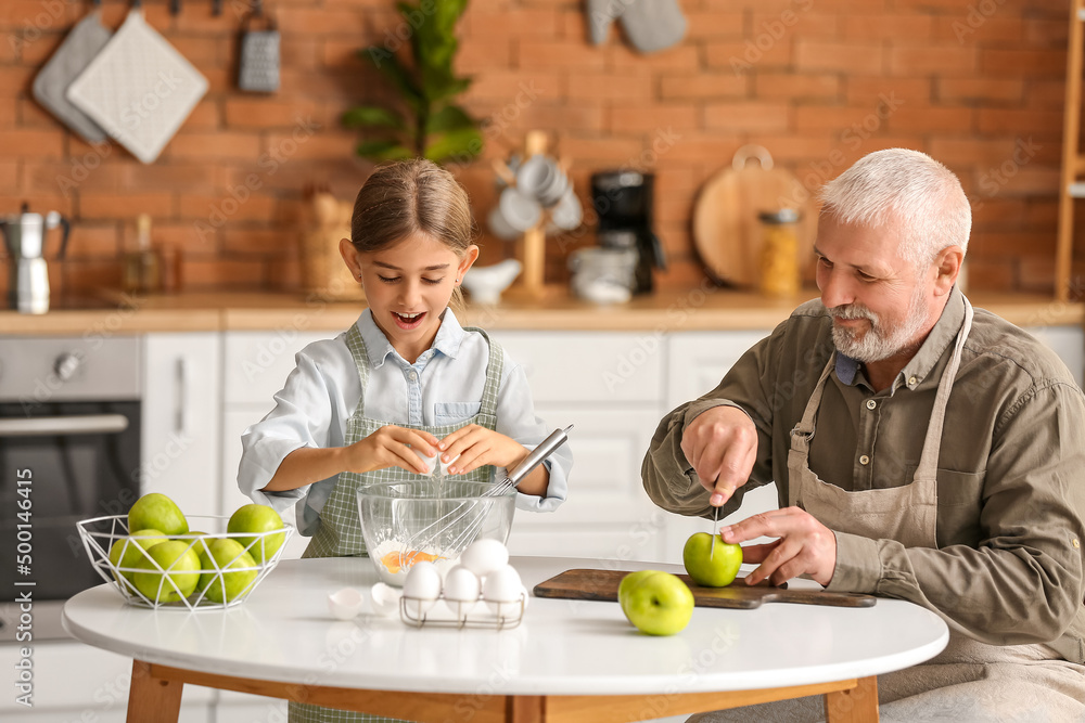 Little girl with her grandfather cooking in kitchen