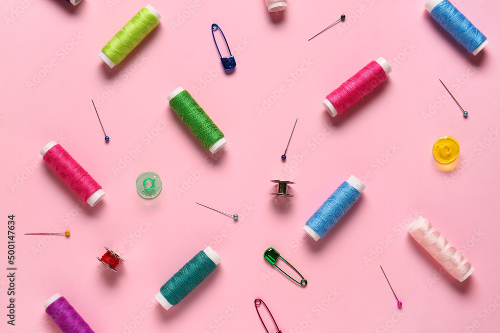 Thread spools and ball pins on pink background