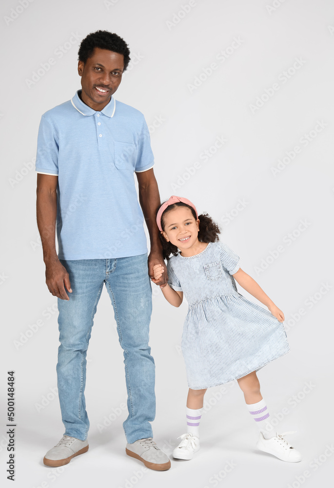 Portrait of little African-American girl and her father on grey background