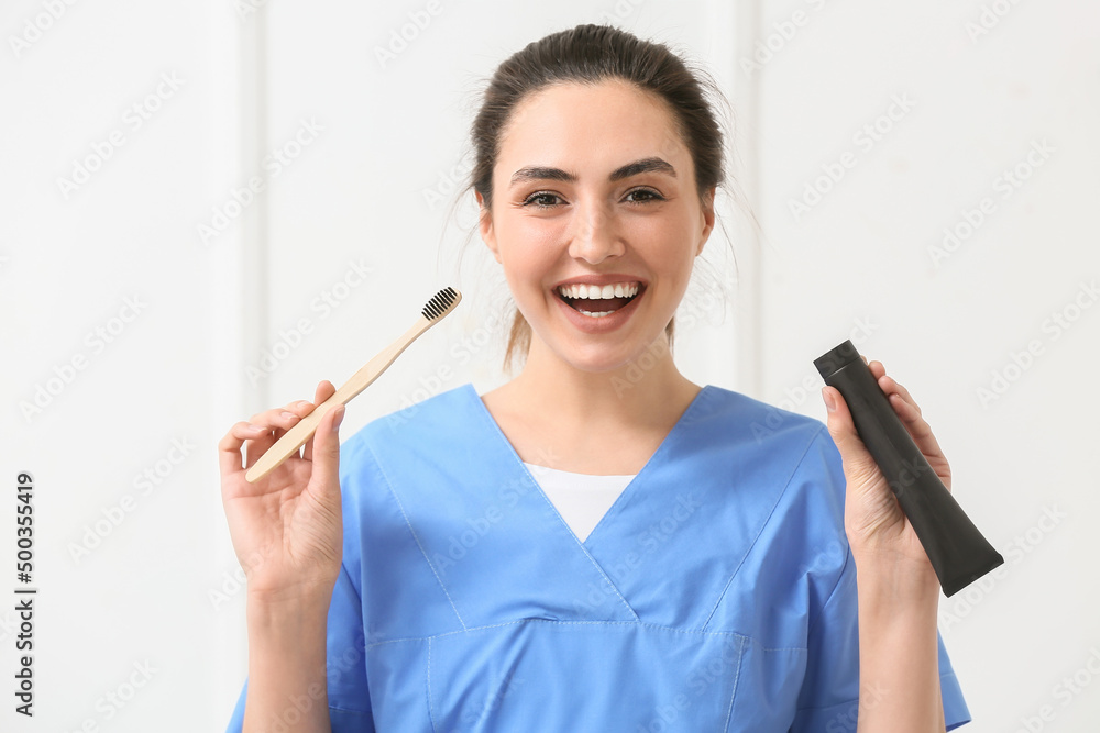 Female dentist with activated charcoal tooth paste and brush on light background