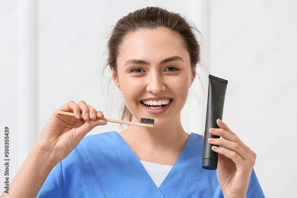 Female dentist with activated charcoal tooth paste and brush on light background