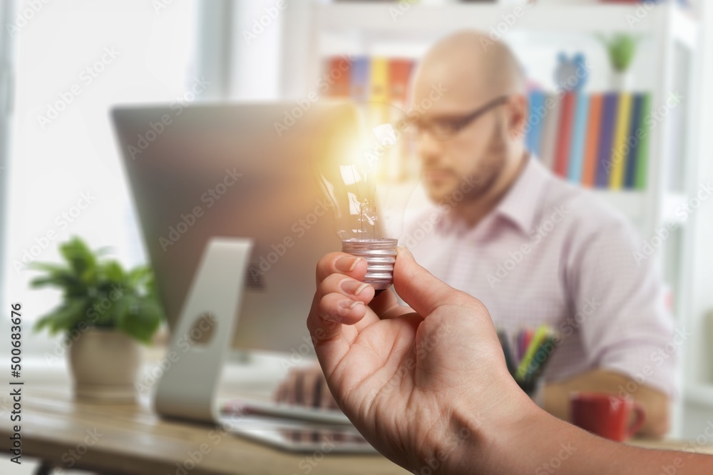 Human hand holds light bulb on workplace background. Save energy concept.