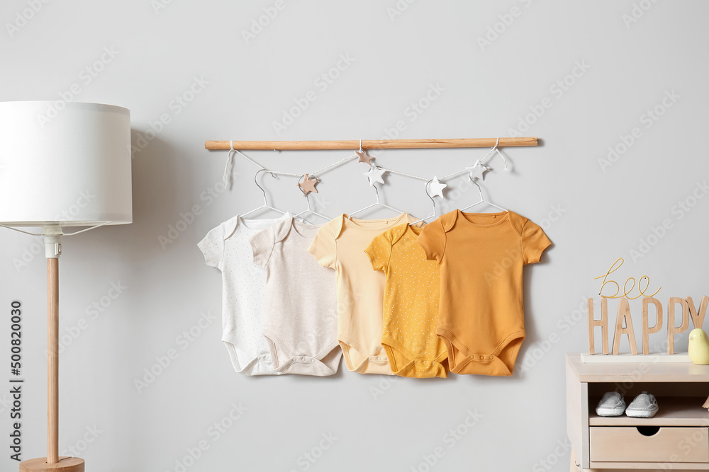 Baby bodysuits hanging on light wall in childrens room