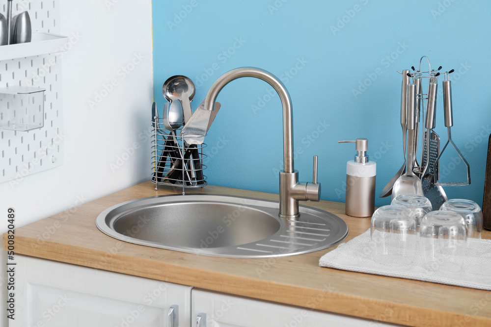 Wooden counter with silver sink and cookware near color wall in kitchen