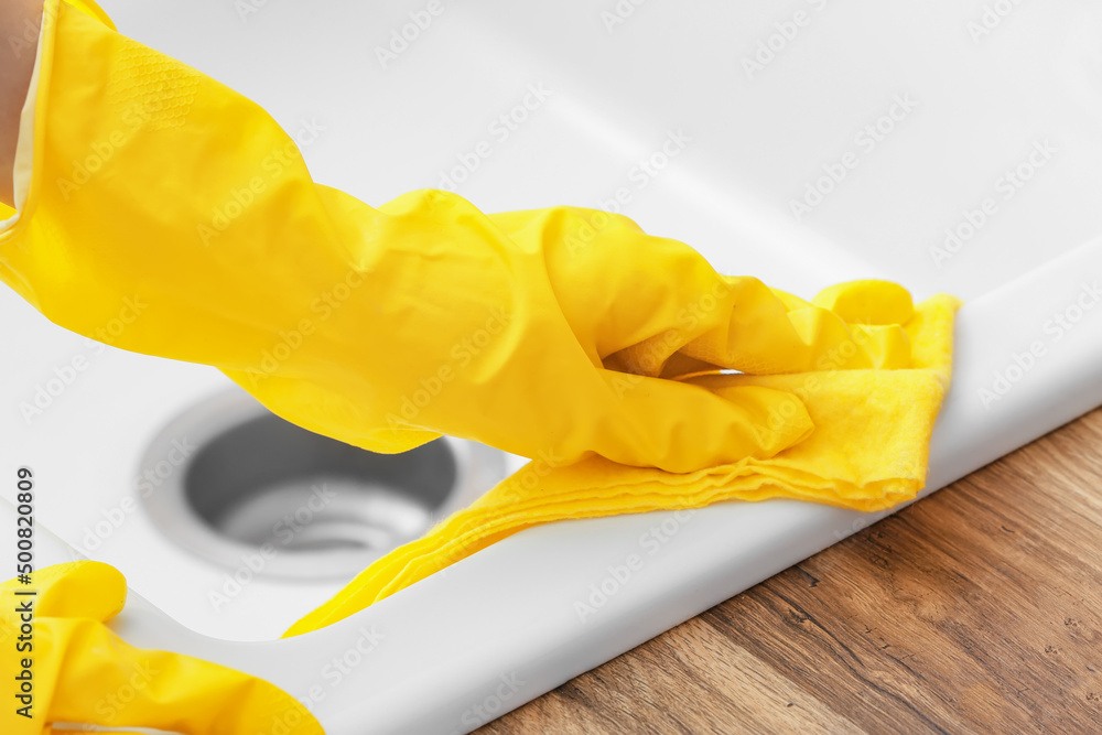 Woman in rubber glove cleaning white sink with sponge, closeup