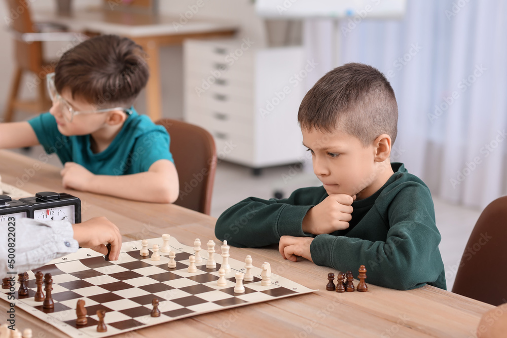 Little children playing chess during tournament in club