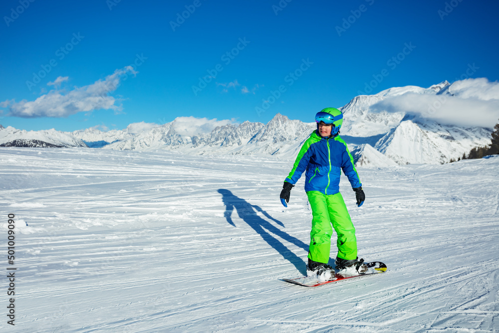 Child go downhill on snowboard high in the mountains