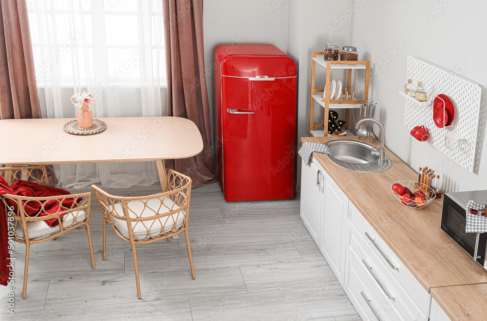 Interior of light kitchen with retro fridge, white counters and dining table