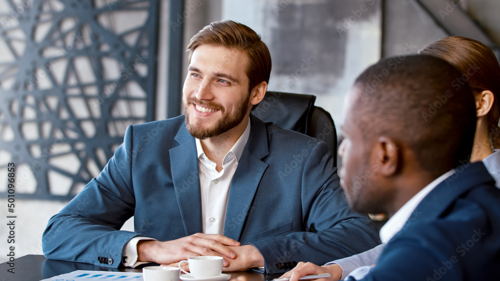 Young man in a suit listening to a corporate leader at a meeting