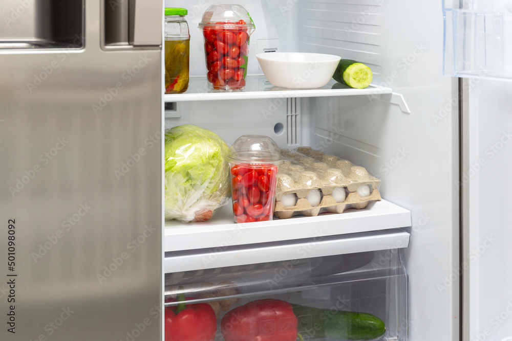 An open fridge in the house with shelves full of vegetables