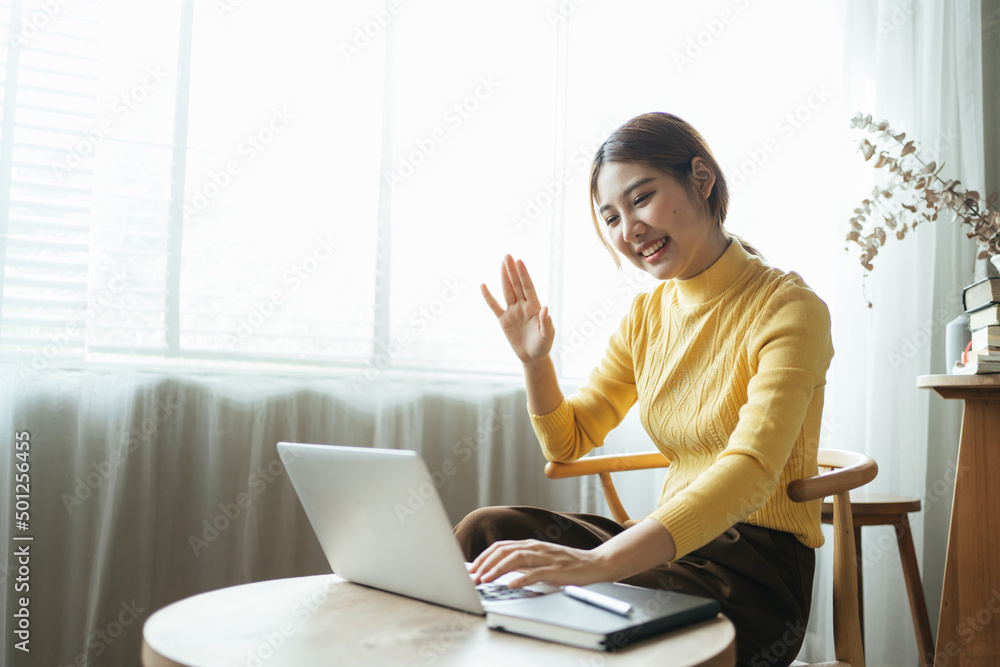 一名亚洲女子在家里的电脑上进行视频通话。一个微笑的女孩在网上和老师学习。