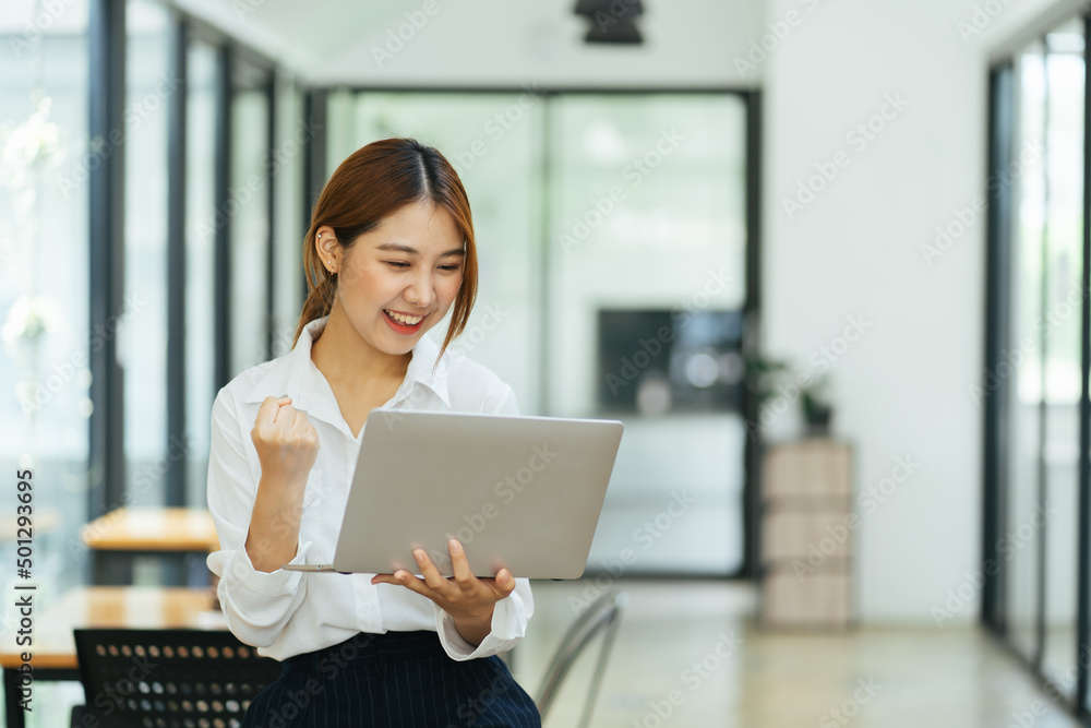 年轻女性拿着笔记本电脑在家办公时表达兴奋，兴奋的亚洲女性感到愉悦