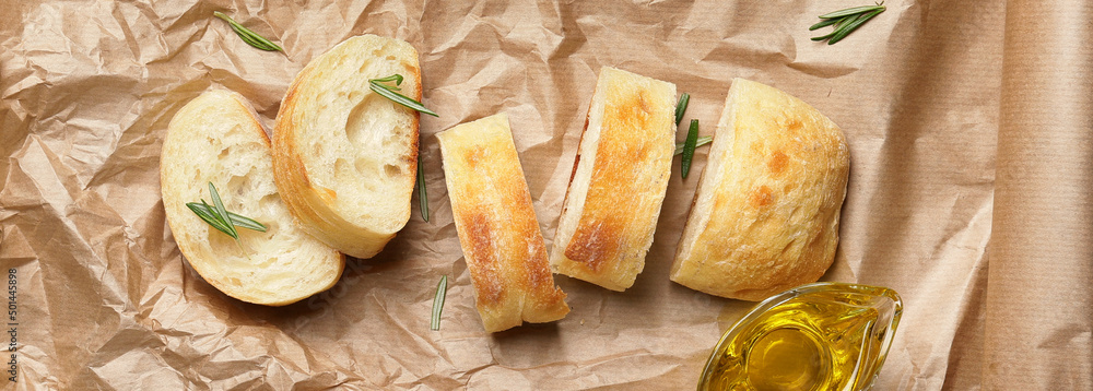 Slices of fresh bread and gravy boat of tasty olive oil on parchment, top view