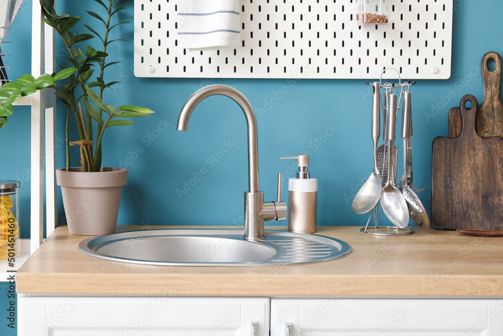 Wooden counter with silver sink, cookware, houseplant and dish soap near blue wall in kitchen