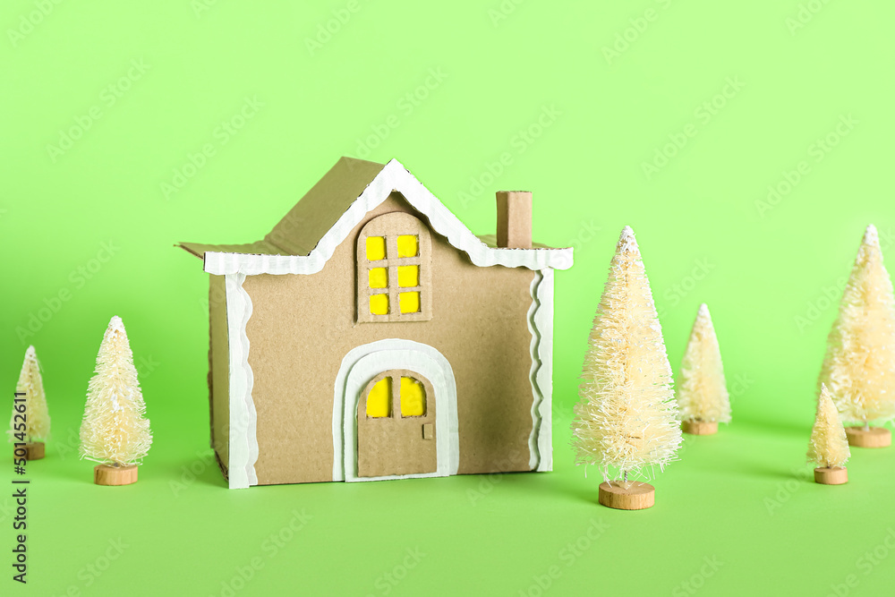 Cardboard house with fir trees on green background