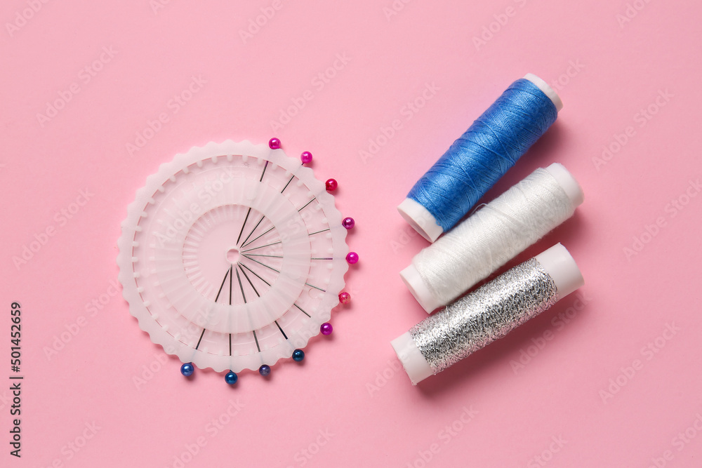 Thread spools and ball pins on pink background