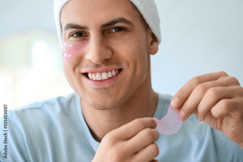 Handsome man applying under-eye patch in bathroom, closeup