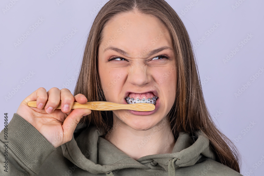 Portrait of young female with braces brushing teeth. Dental concept.