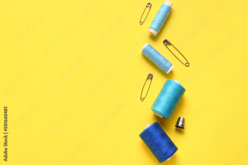 Thread spools and pins on yellow background