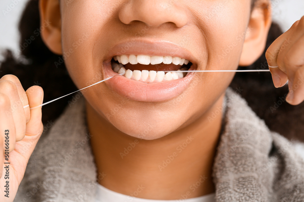 African-American teenage girl flossing teeth on light background, closeup