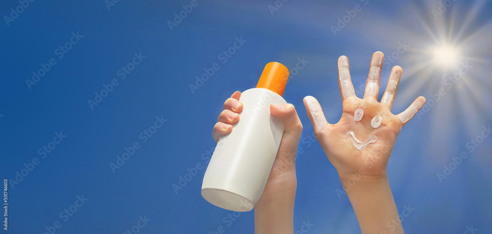 Positive symbol drawing by sunscreen on open hand. Another hand holding a bottle of sun cream. Sky, 