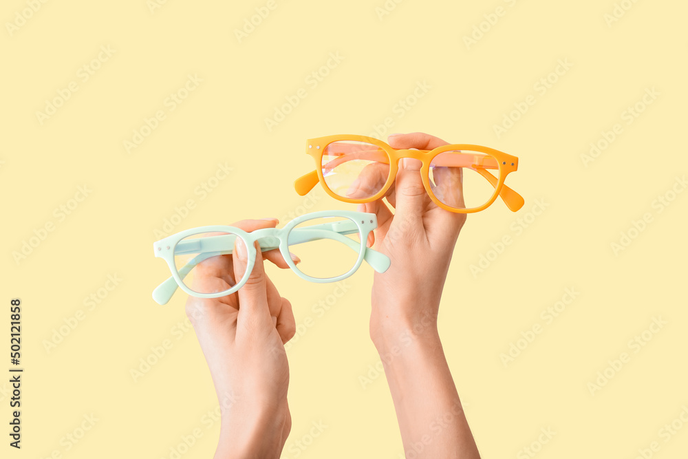 Female hands with different eyeglasses on yellow background