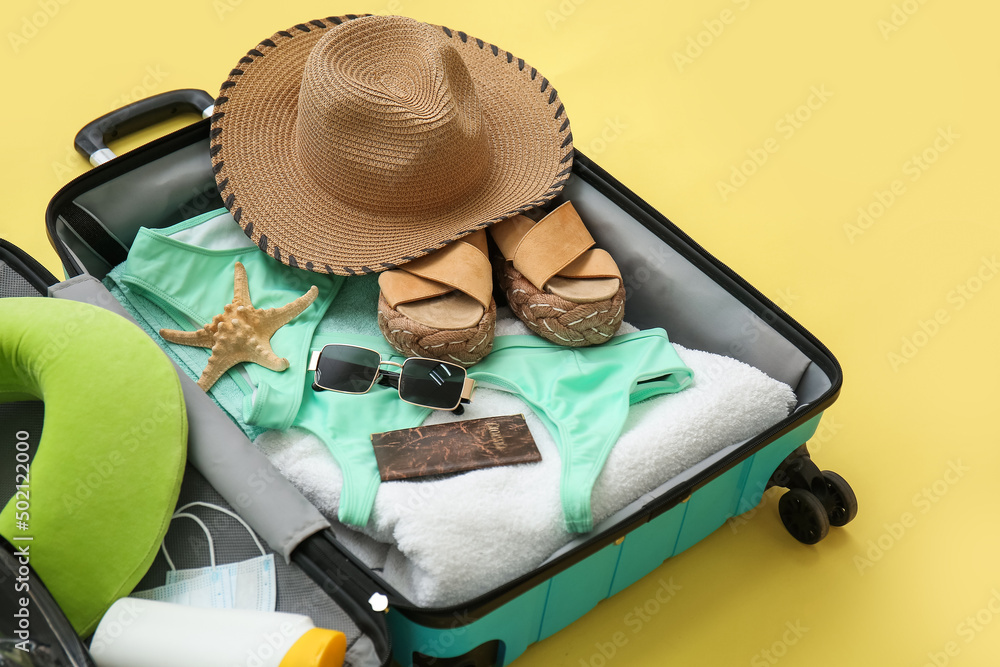 Suitcase with female beach accessories and snorkeling mask on yellow background