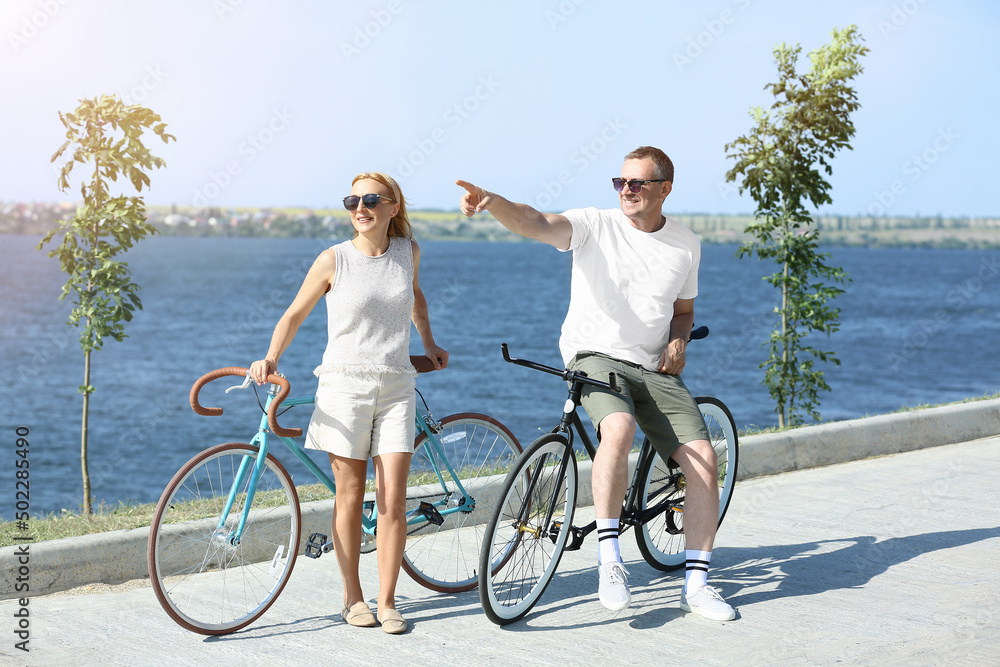 Mature couple with bicycles walking along river bank on summer day