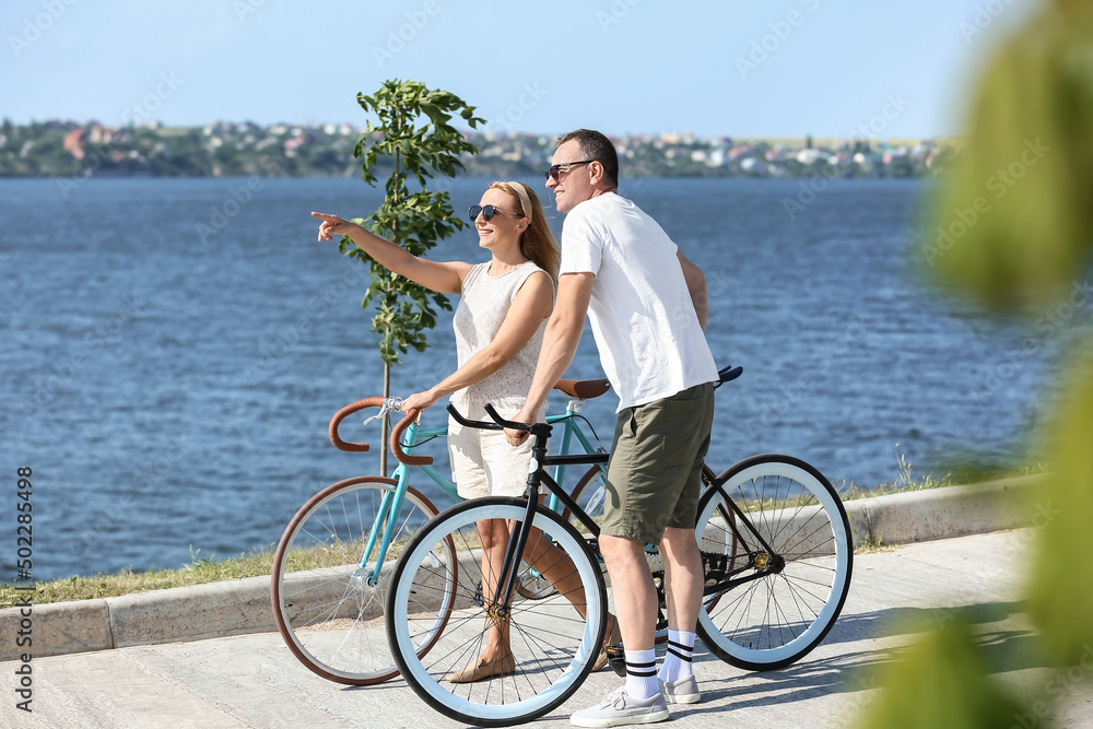 夏日，一对骑着自行车沿着河岸散步的成熟夫妇