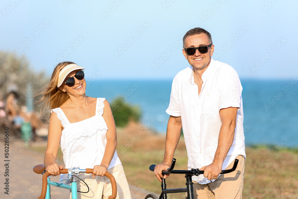 Mature couple with bicycles walking along sea shore on summer day